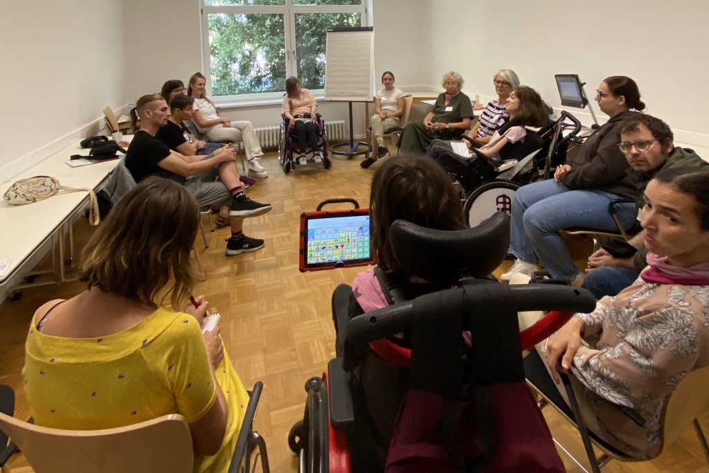 Eine Gruppe von Menschen mit und ohne Behinderung sitzen bei einer Fortbildung in einem Kreis.