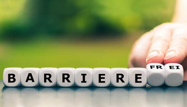 Das Bild zeigt das Wort „Barrierefrei“ auf Würfeln. Die Würfel mit dem Wort „Frei“ werden von einer Hand leicht nach hinten gekippt