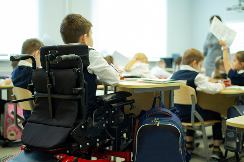 Junge sitzt im Rollstuhl in einer Schulklasse und arbeitet im Unterricht mit.